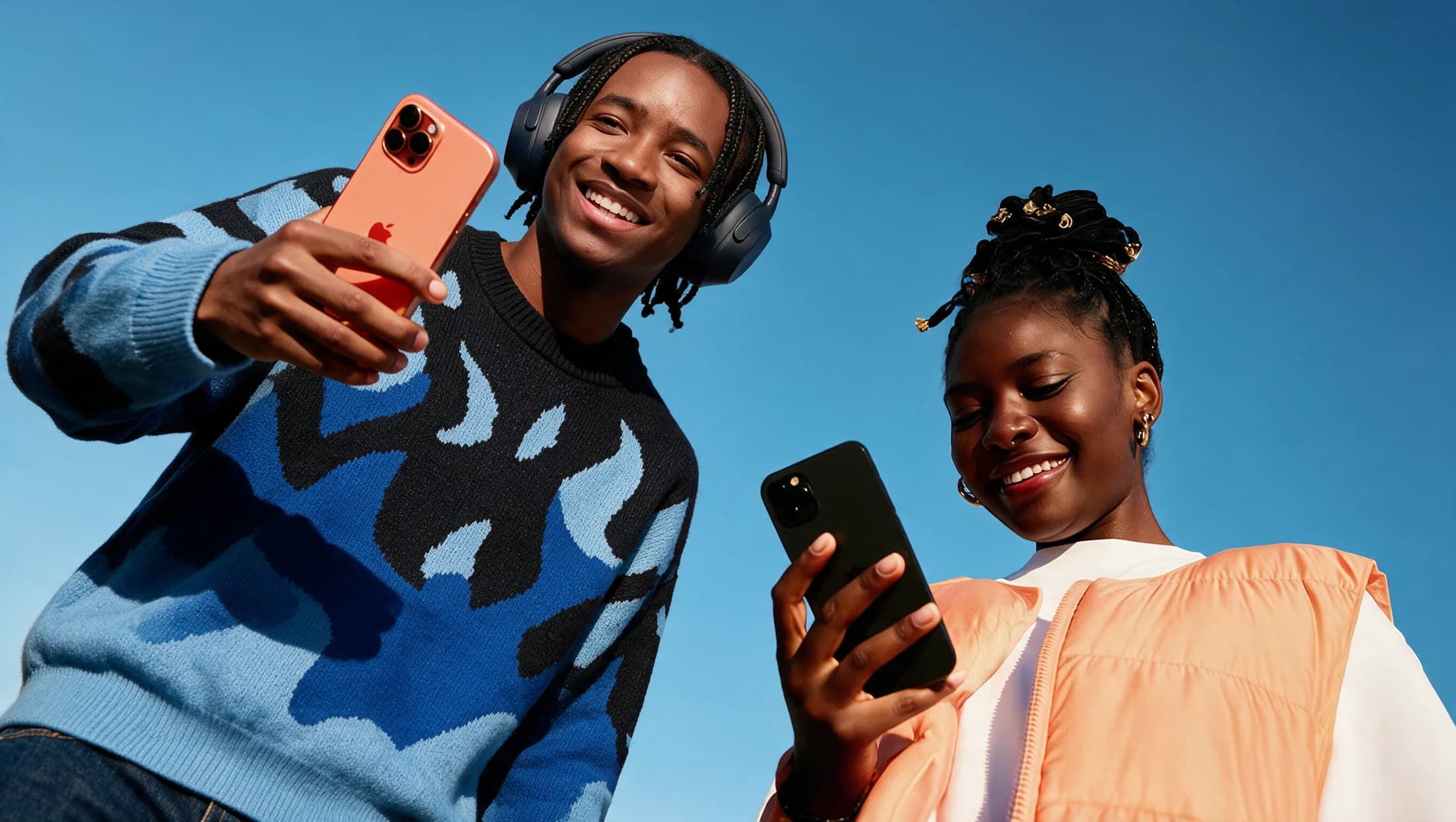 Two smiling players holding their phones against a bright blue sky.